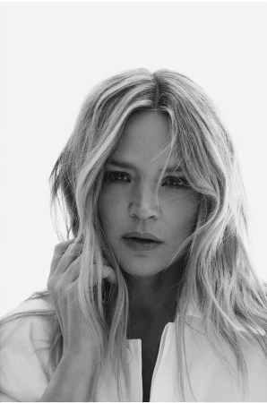 Monochrome portrait of a woman with blonde hair wearing a white collared shirt against a plain bright background.