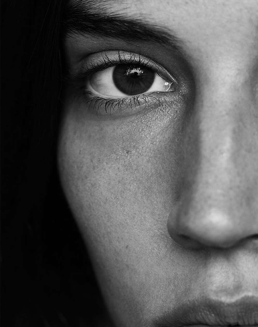 Extreme close-up monochrome portrait focusing on a person's eye, nose, and cheek with visible skin texture