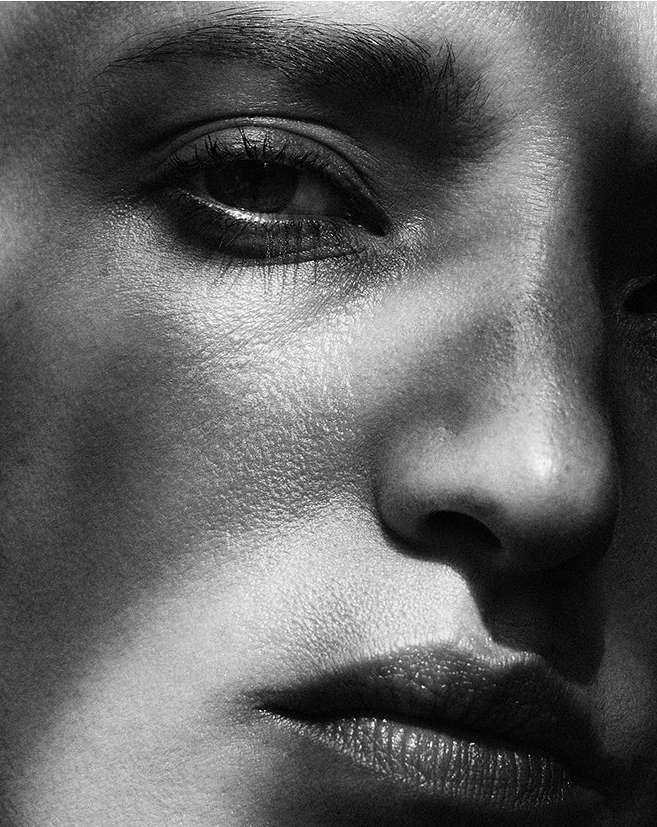 Monochrome close-up of a woman's face featuring dramatic lighting, highlighting facial features like the eye, nose, and lips.