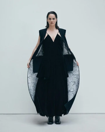 Model wearing a black velvet dress and sleeveless coat against a plain white studio background.