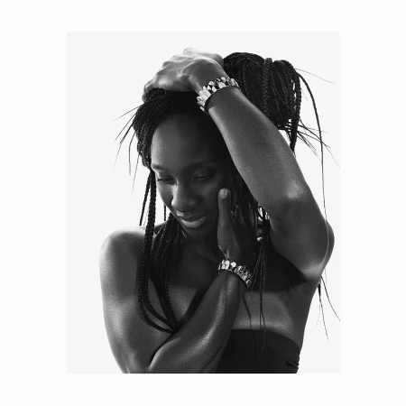 Black and white portrait of a black woman wearing metallic bracelets, with long braided hair, posing against a white background.