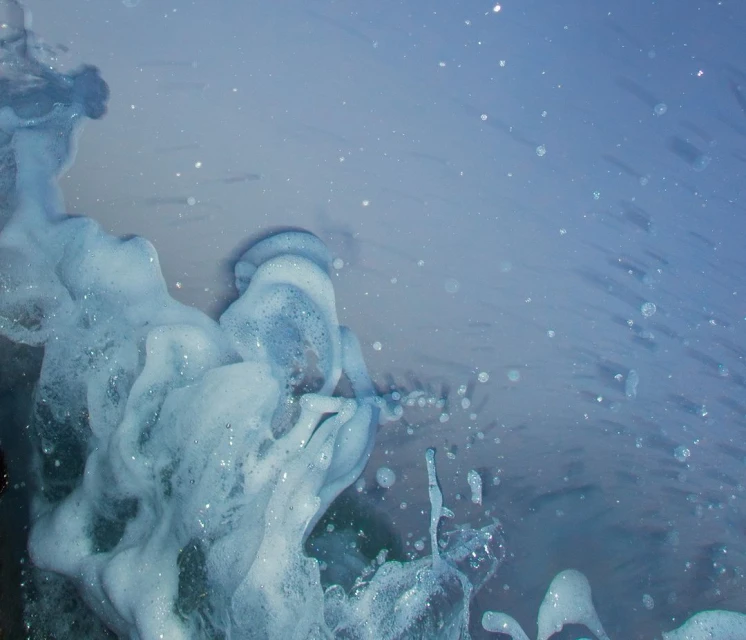 Close-up of splashing blue water with white foam, creating a dynamic and textured scene of fluid motion and light reflection.