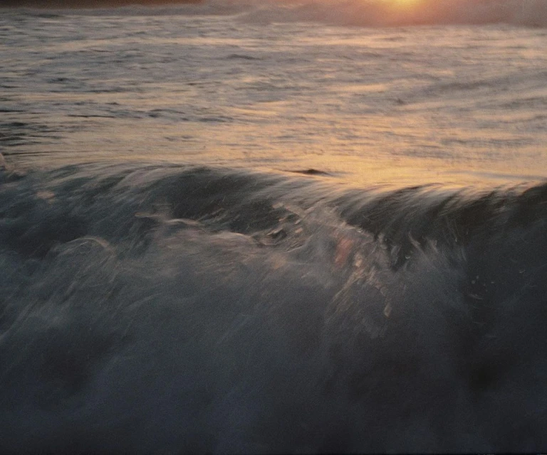 Ocean waves crashing at sunset, creating a serene and dynamic seascape with golden light reflecting on the water's surface.