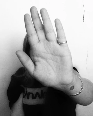 Close-up of a person holding an open hand up to block the camera lens, wearing a ring and bracelet.