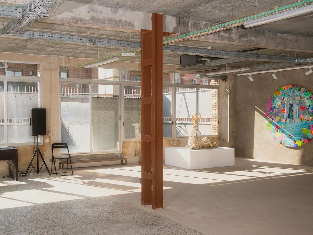 Bright, airy gallery space features an abstract art installation with modern art, speaker, chair, and natural light from large windows.