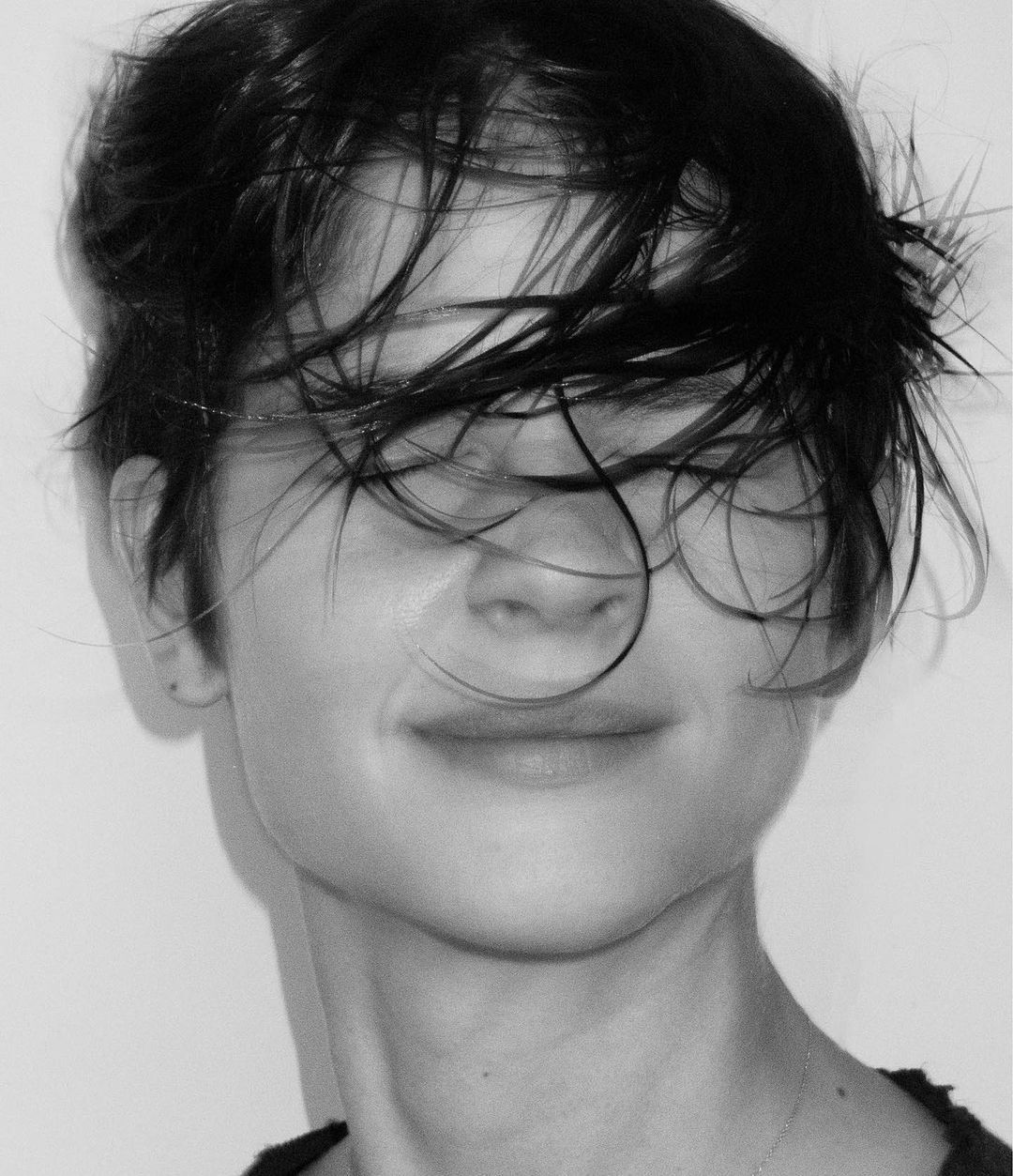 Close-up monochrome portrait of a person with dark wet hair covering their eyes against a plain white background.