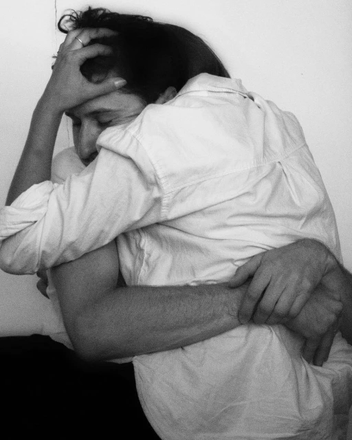 A close-up black and white photo features two adults embracing, one with a hand on their head, set against a plain white background.