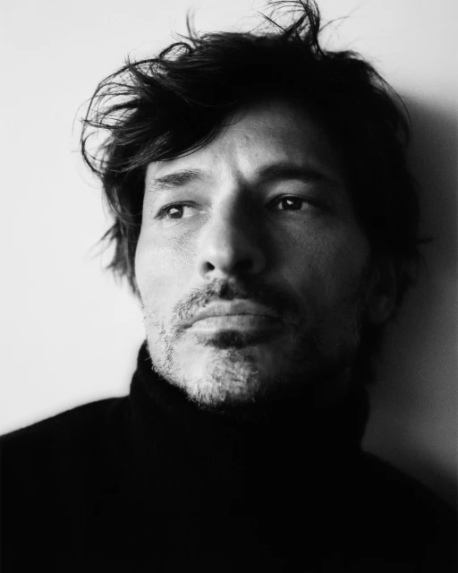 Portrait of a man with dark hair wearing a turtleneck sweater against a light background in black and white, close-up shot.