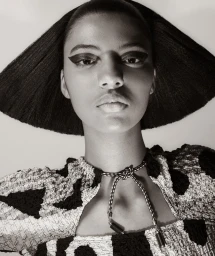 Close-up portrait of a woman with dramatic winged eyeliner wearing a black and white patterned top and a sculpted hat.
