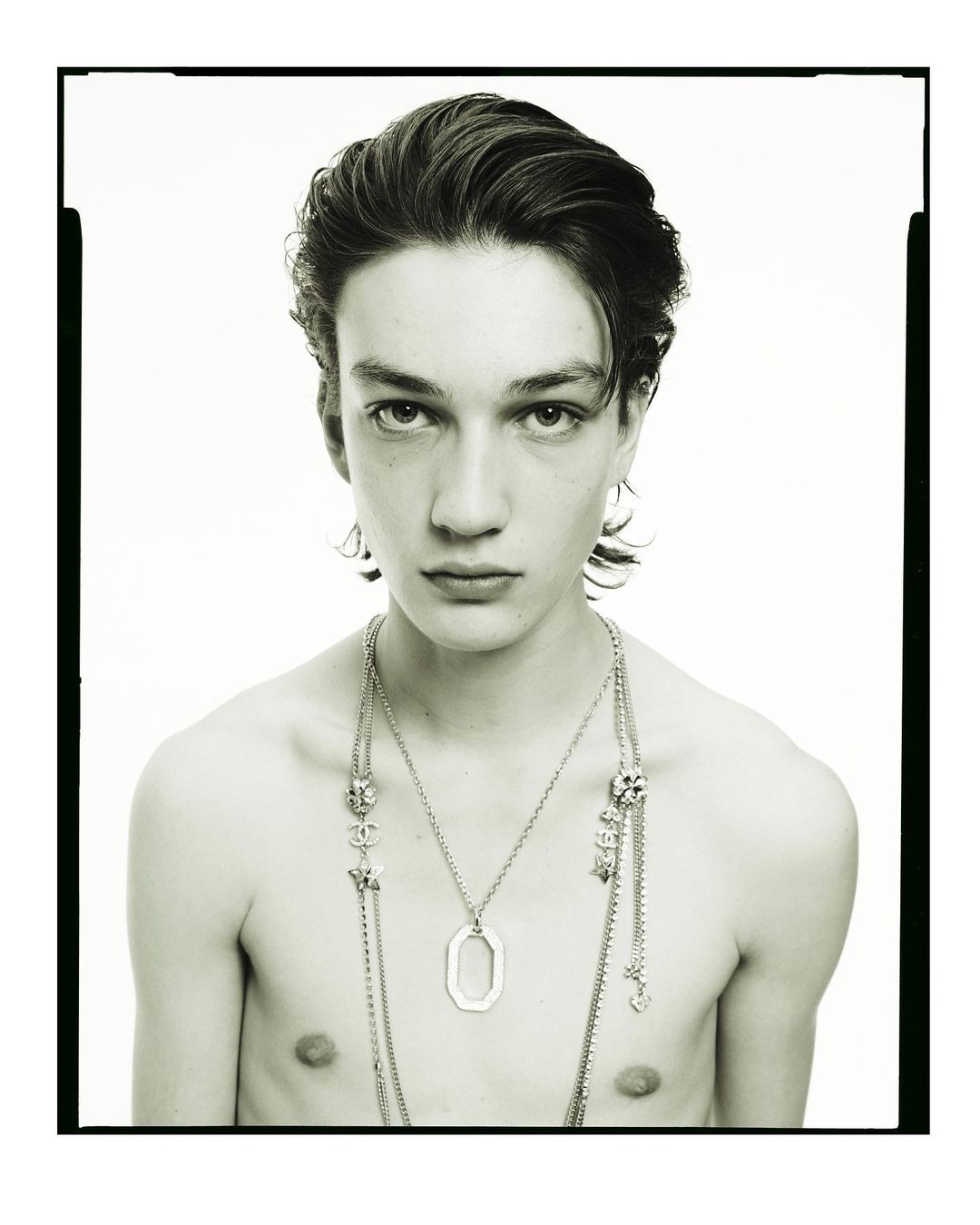 Portrait of a young man wearing layered silver pendant necklaces against a plain white background by photographer Pablo Di Prima.
