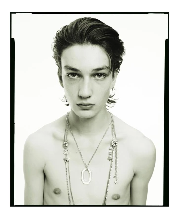 Portrait of a young man wearing layered silver pendant necklaces against a plain white background by photographer Pablo Di Prima.