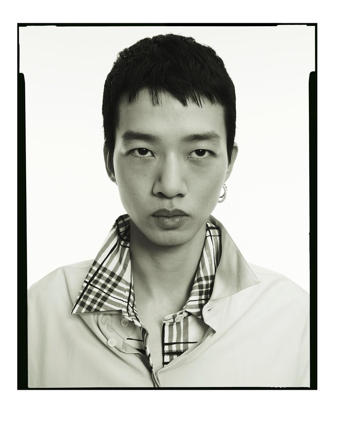 Monochromatic portrait of a young adult male with short dark hair, wearing a light shirt with a plaid collar, captured in a photo studio.