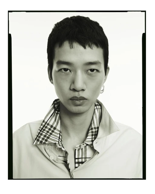 Monochromatic portrait of a young adult male with short dark hair, wearing a light shirt with a plaid collar, captured in a photo studio.