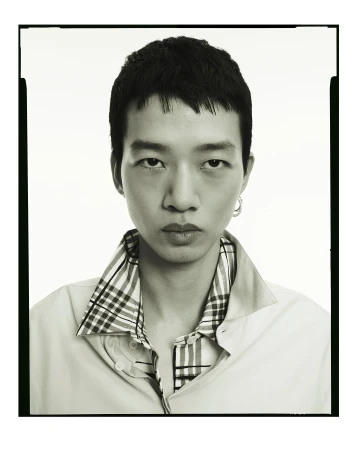 Monochromatic portrait of a young adult male with short dark hair, wearing a light shirt with a plaid collar, captured in a photo studio.