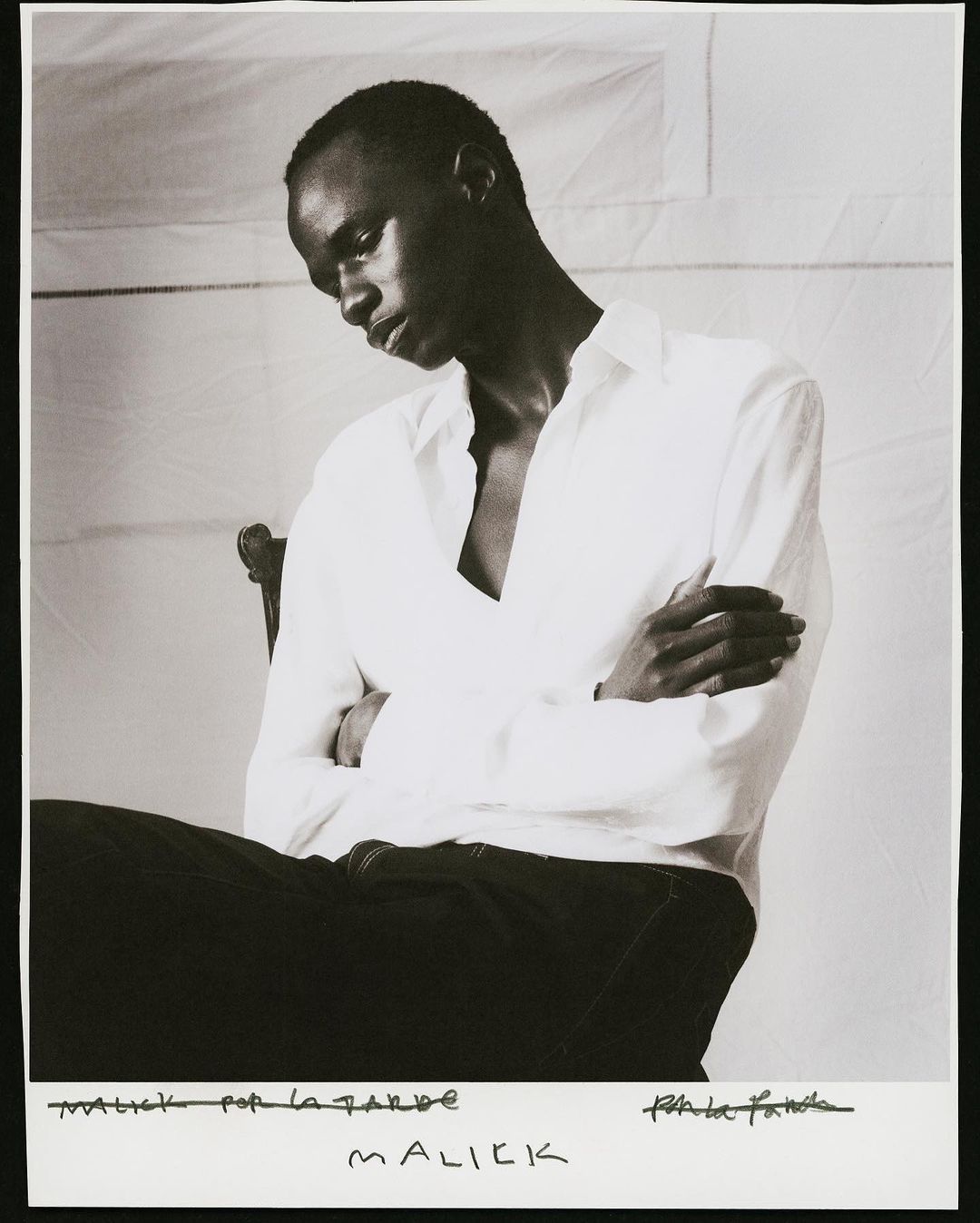 Monochrome portrait of a black man with crossed arms wearing a white shirt against a white backdrop.