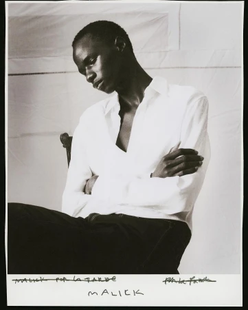 Monochrome portrait of a black man with crossed arms wearing a white shirt against a white backdrop.