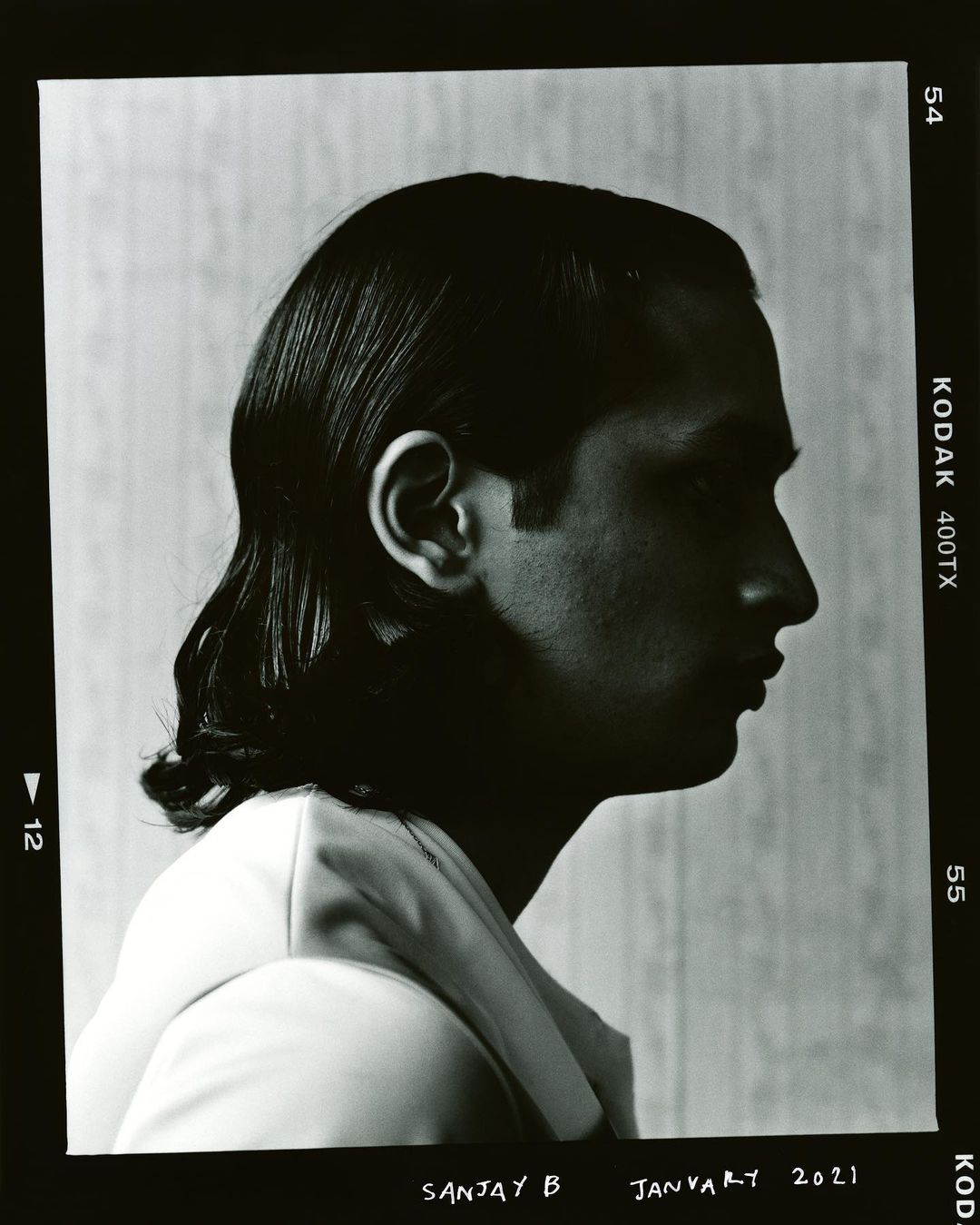 Monochrome portrait of a man in profile wearing a suit, captured in a film photograph with visible frame edges, showing his side face and hair.