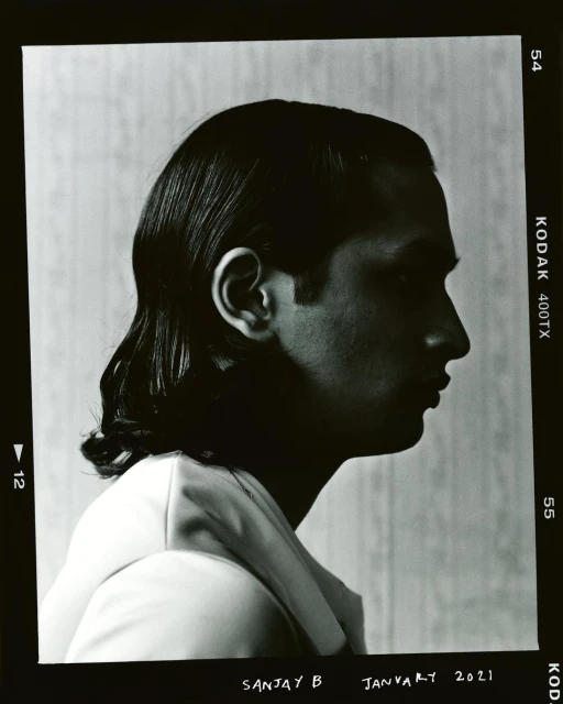 Monochrome portrait of a man in profile wearing a suit, captured in a film photograph with visible frame edges, showing his side face and hair.