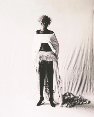 Monochrome portrait of a model with short textured hair wearing an off-the-shoulder white top and a long sheer overlay skirt