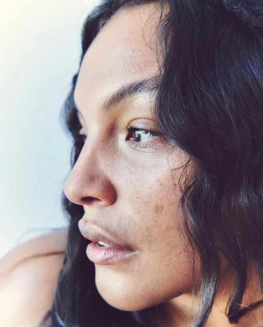 Portrait of an adult woman with dark hair, side profile view, against a soft white background in natural lighting.