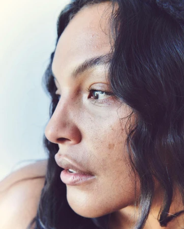 Portrait of an adult woman with dark hair, side profile view, against a soft white background in natural lighting.