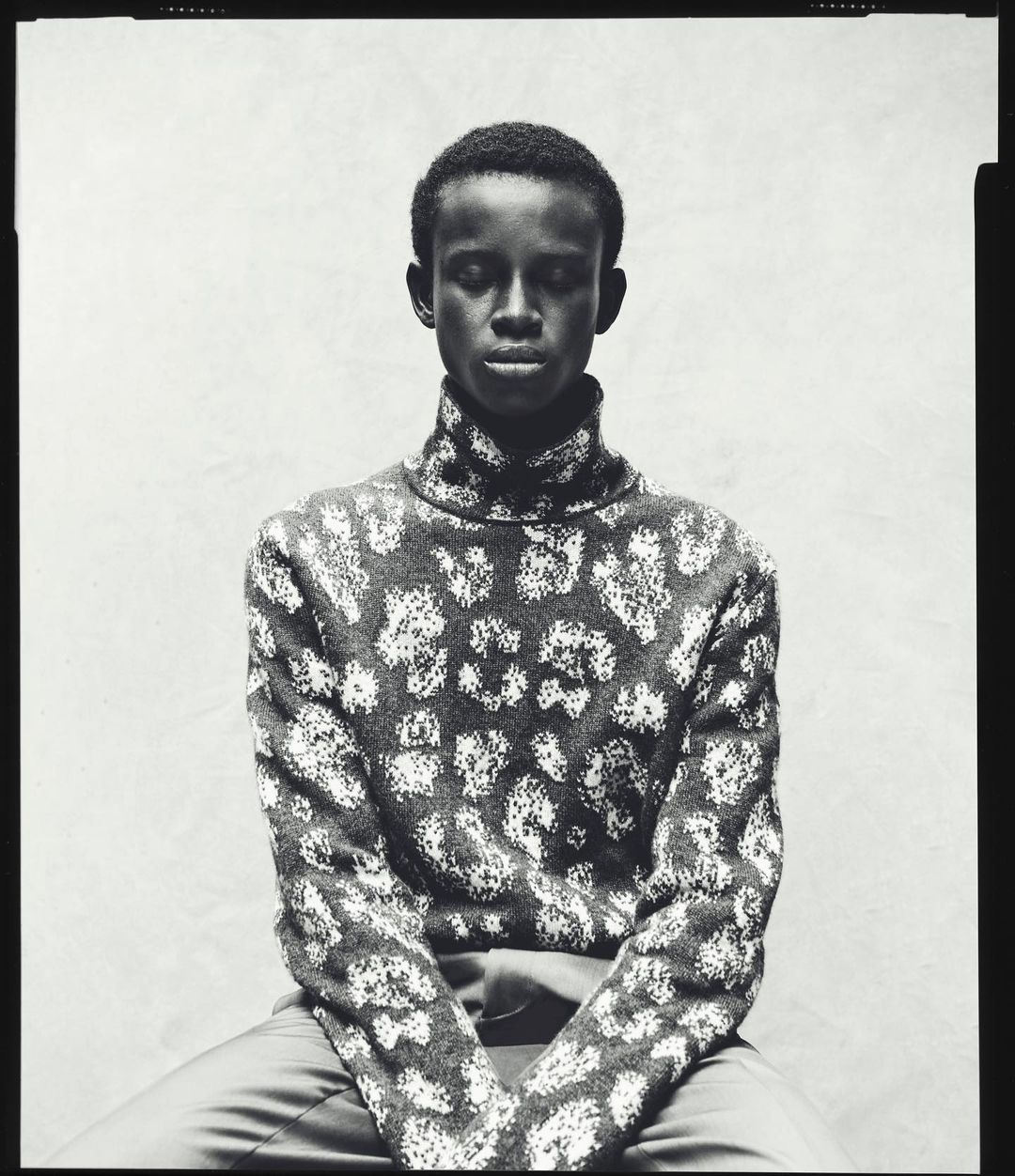 Portrait of a Black man with short hair wearing a patterned turtleneck sweater, photographed in black and white by Pablo Di Prima.