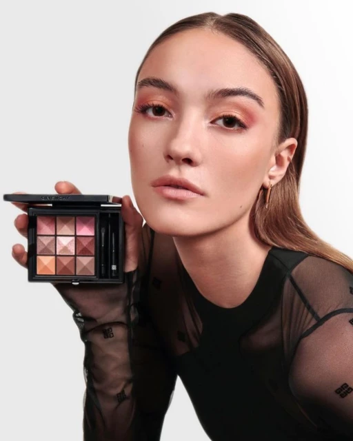 Woman displays Givenchy eyeshadow palette in studio shot with pink, brown, and copper tones, light skin, and sheer black top.