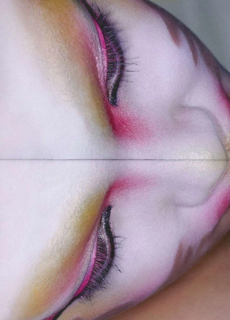 Close-up of a woman's face with pink and gold eye makeup, featuring long, dark eyelashes, captured with a soft, diffused lighting.