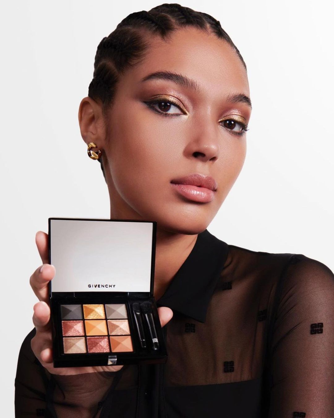 Elegant woman with golden eyeshadow presents a makeup palette in a studio setting, showcasing beauty and cosmetic product.