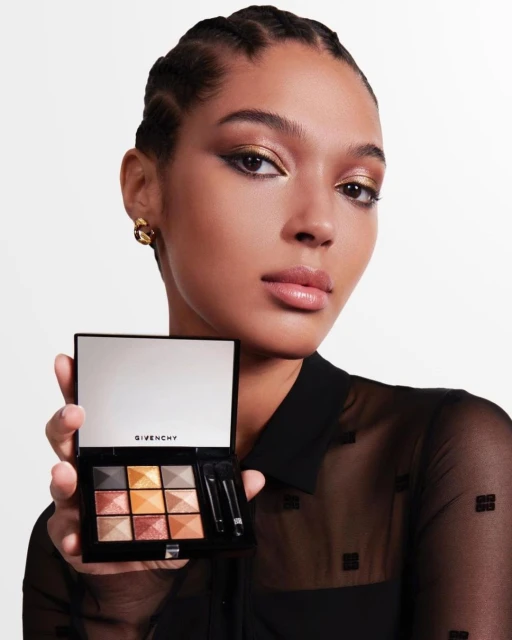 Elegant woman with golden eyeshadow presents a makeup palette in a studio setting, showcasing beauty and cosmetic product.