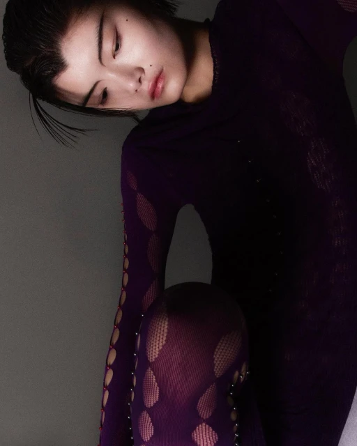 Portrait of a young Asian woman in a purple patterned top and leggings, posed against a grey backdrop in a beauty fashion photograph.