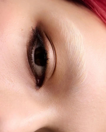 Close-up shot of an adult female's eye with brown iris and dark lashes, fair skin, and pink hair, possibly in a beauty or fashion context.