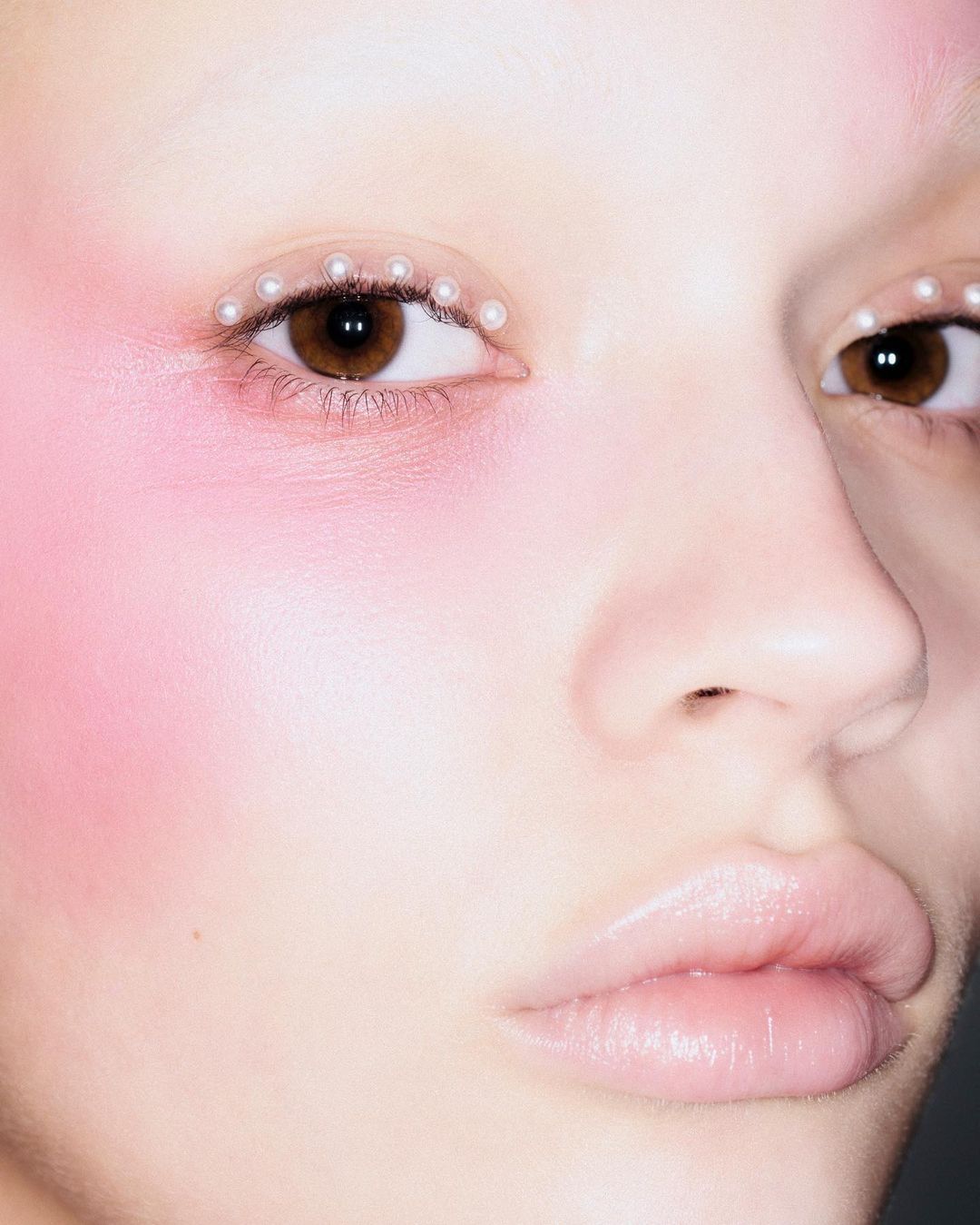 Close-up of a woman with pink blush and pearl accents around the eyes in a beauty shot highlighting makeup and skin.