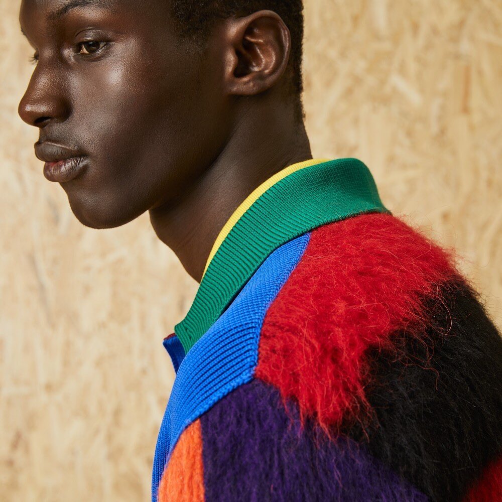 Close-up of an African American male model in a colourful, patterned sweater, set against a plain wooden background.