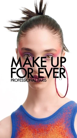 A woman is centered in a portrait wearing colorful eyeshadow and a blue and orange top. The background is white, and hoop earrings are visible.