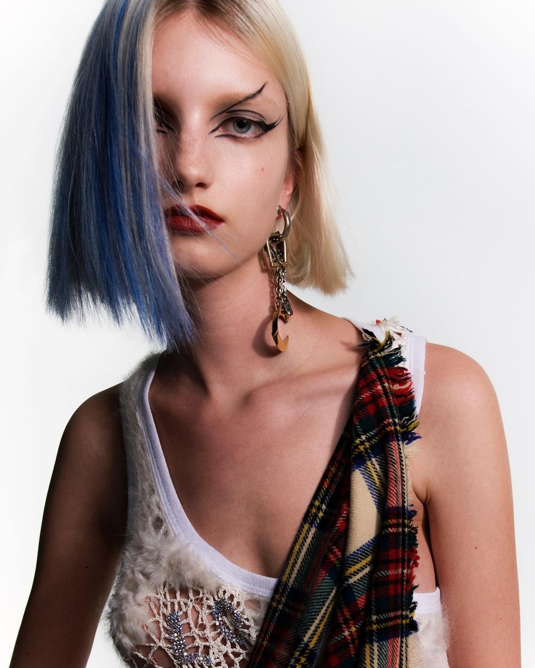 Close-up studio portrait of a young, fair-skinned woman with platinum blonde hair with a streak of blue and dramatic eye makeup.