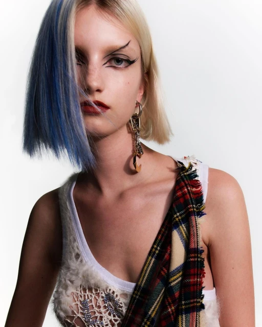 Close-up studio portrait of a young, fair-skinned woman with platinum blonde hair with a streak of blue and dramatic eye makeup.