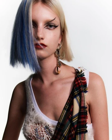 Close-up studio portrait of a young, fair-skinned woman with platinum blonde hair with a streak of blue and dramatic eye makeup.