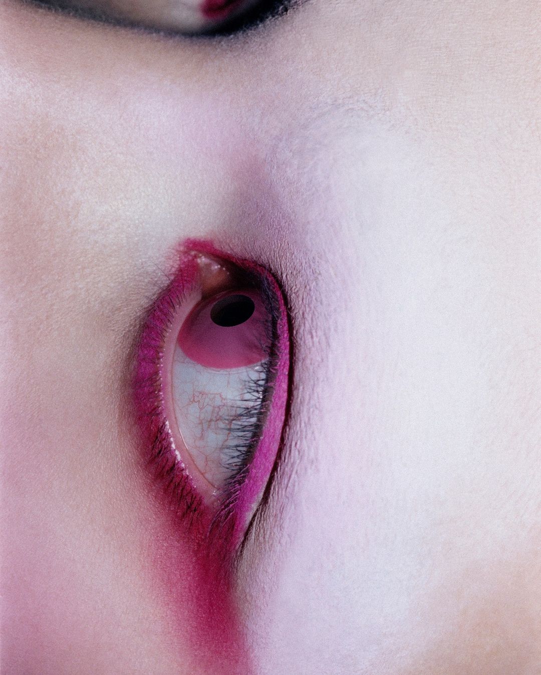 Close-up of a woman's face with creative pink makeup accentuating a surreal eye and lip transformation for a beauty or fashion concept.