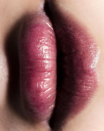 Close-up of an adult female's lips, showcasing their texture, color, and shape, set against a fair skin tone background in a macro photography style.