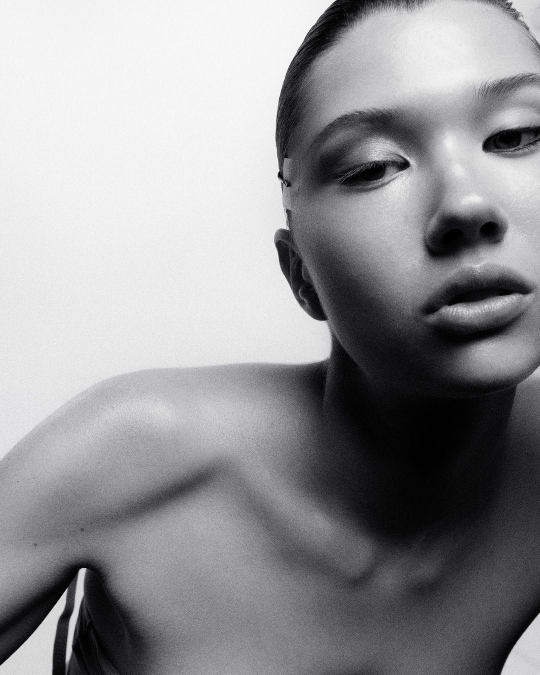 Close-up monochrome portrait of a woman looking down against a bright white background, photographed in Paris by Pablo Freda.