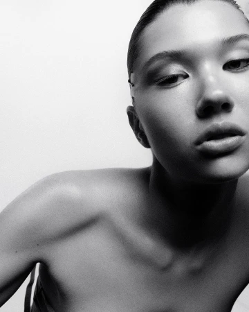 Close-up monochrome portrait of a woman looking down against a bright white background, photographed in Paris by Pablo Freda.