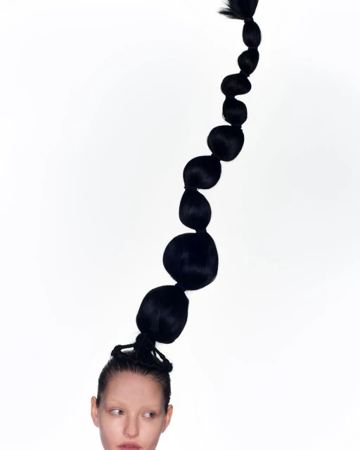 Headshot of a fair-skinned person with black sculptural ponytail hairstyle on a white background, creating a minimalist, surreal portrait.
