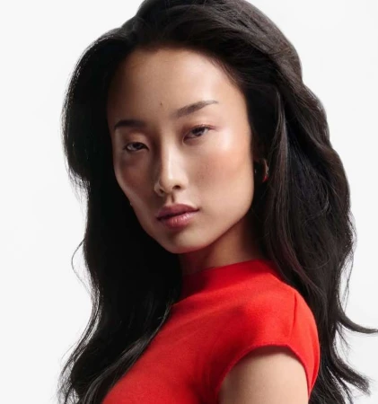 Portrait of an East Asian woman with long dark wavy hair wearing a red top against a white background
