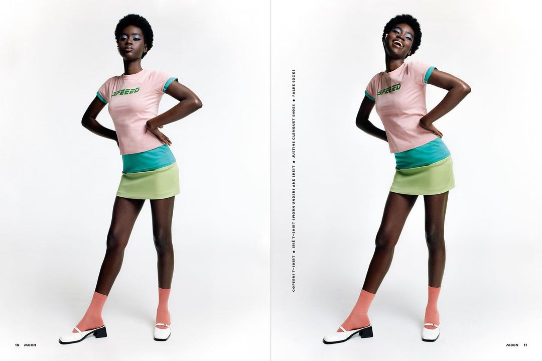A smiling Black fashion model poses in a color-blocked miniskirt outfit against a white backdrop in a studio fashion shot.
