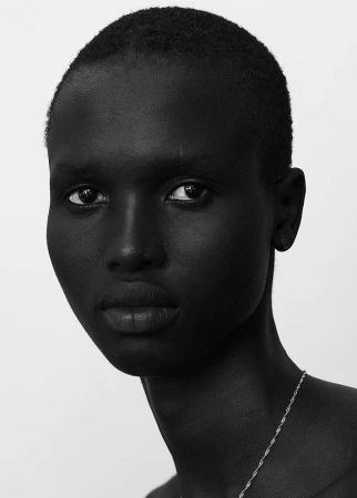 Monochrome portrait of a black man with a buzz cut wearing a thin silver chain necklace against a plain white background.