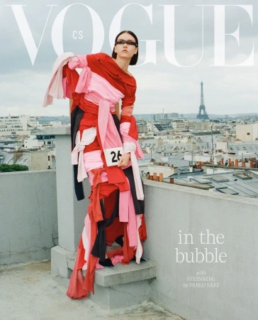 Model wearing a layered red, pink, and black fabric dress on a Parisian rooftop with the Eiffel Tower in the background.