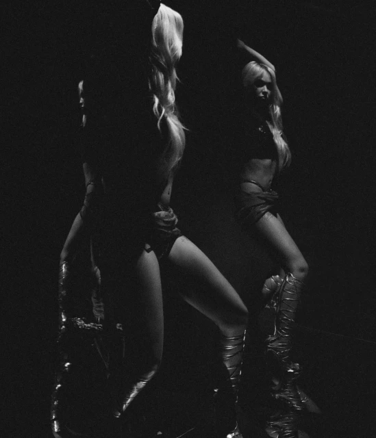 Black and white image of a fair-skinned adult woman in a dark environment, featuring a bare midriff and thigh-high gladiator boots.