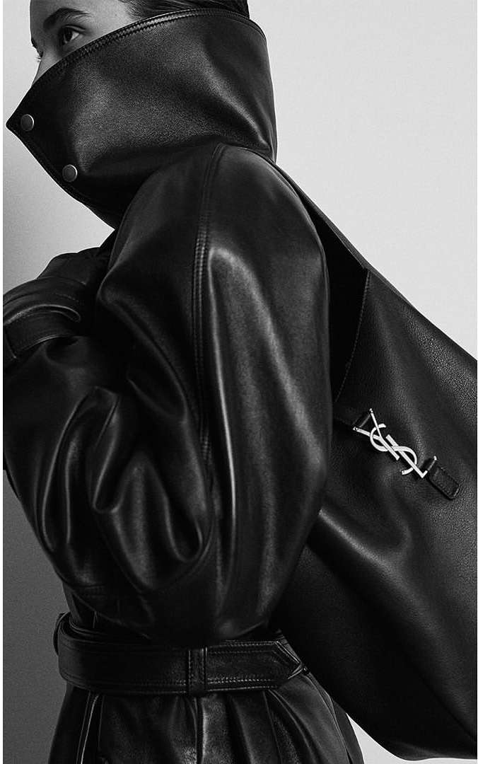 Fashion shot of a woman wearing a black leather coat with a high collar, black leather pants and a black leather purse with a silver logo.