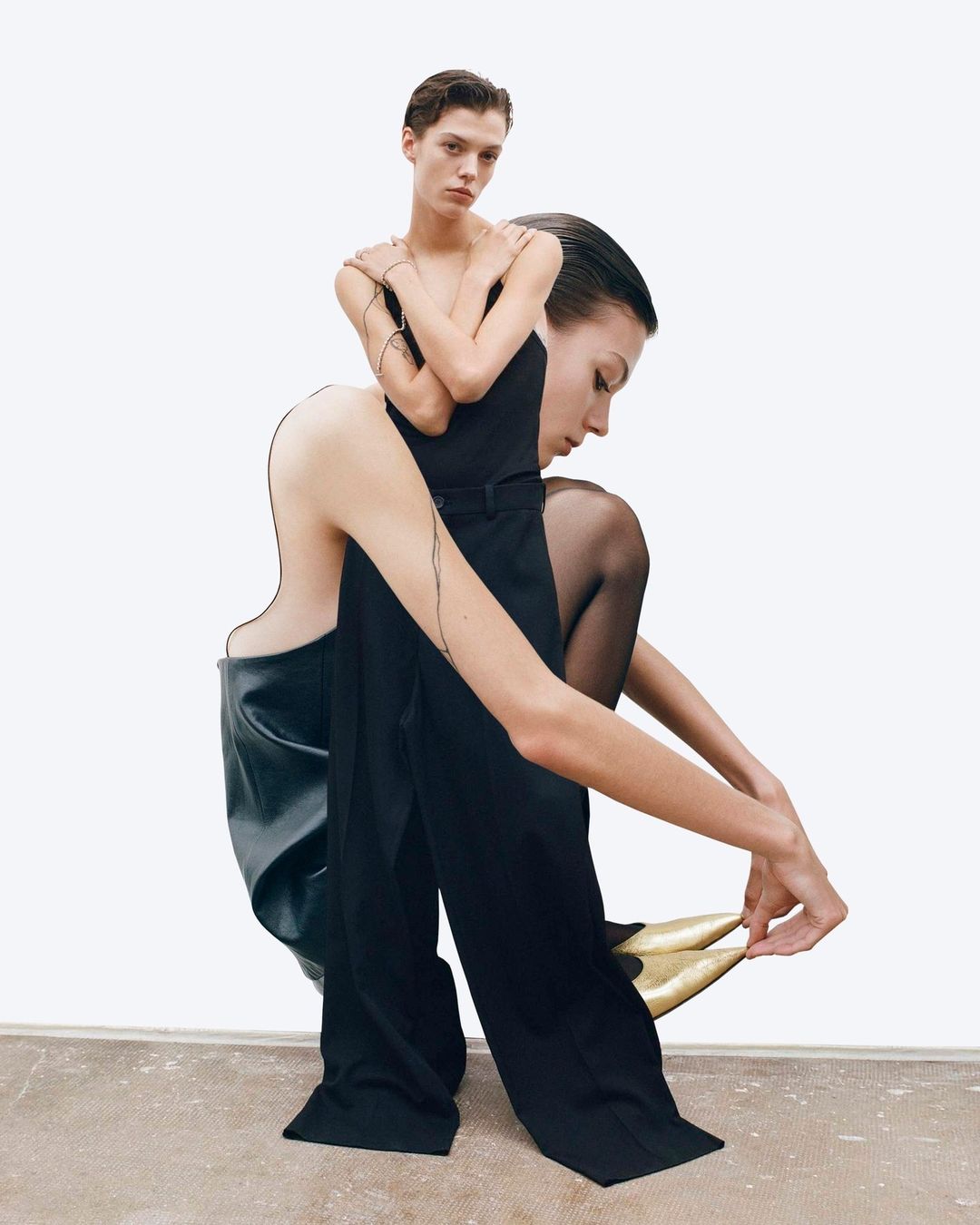Two female models in a collage-style fashion shot. One model sits while another stands, wearing black and gold garments against a white backdrop.